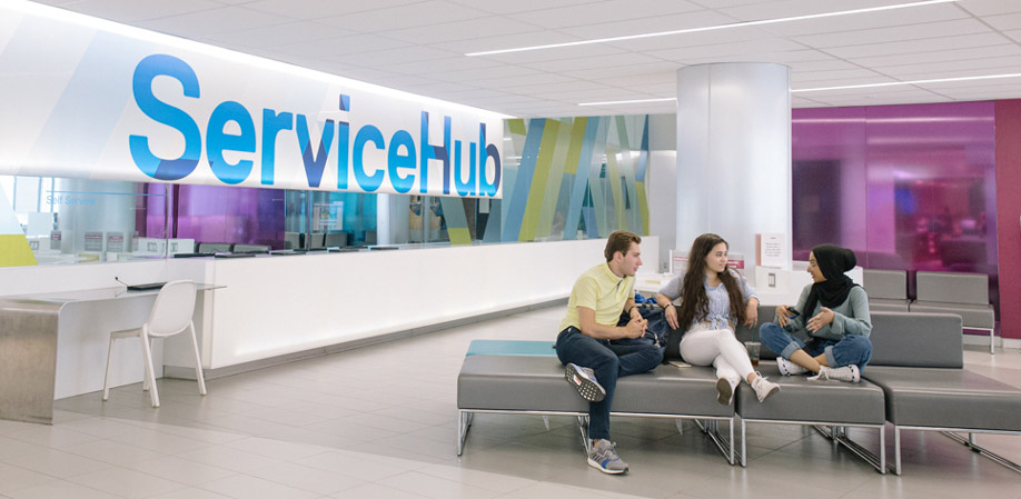 Three students chat animatedly while sitting outside the ServiceHub.