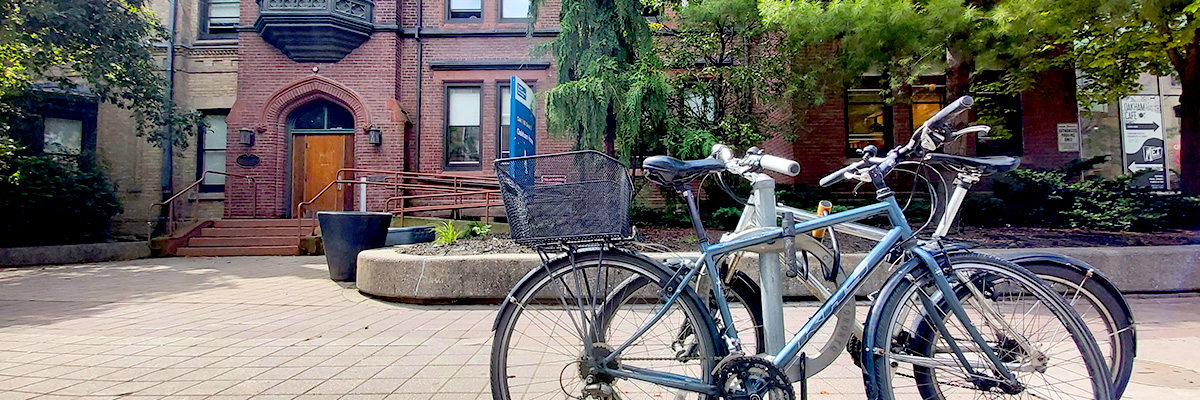 Two bikes are parked at a post-and-ring bike rack in front of historic Oakham House