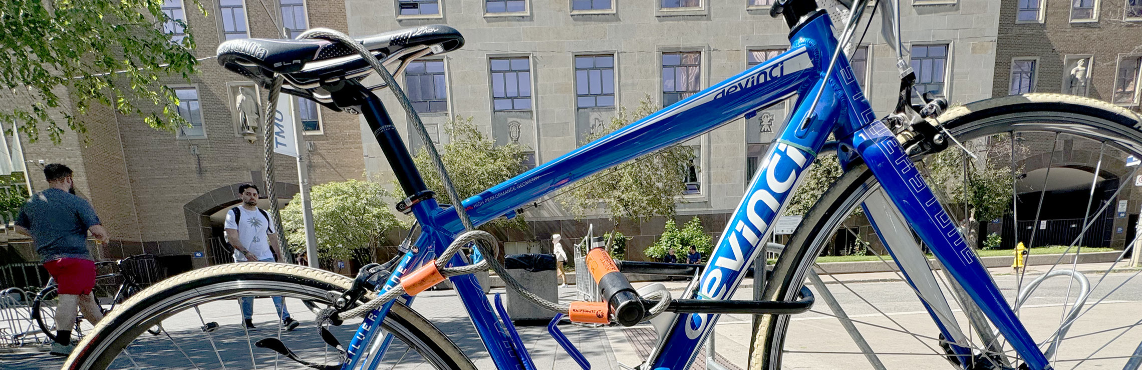 A blue, Canadian-made bicycle is locked to a bike rack on campus with Kerr Hall in the background.