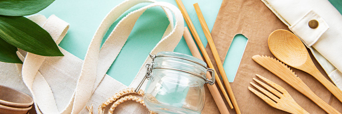 A variety of sustainable, reusable items like stainless steel water bottles and straws, glass bottles and jars and wooden cutlery on a linen tablecloth.