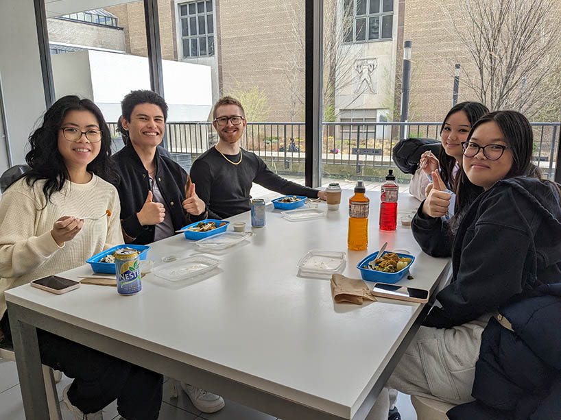 Students sitting at a table eating and smiling with thumbs up