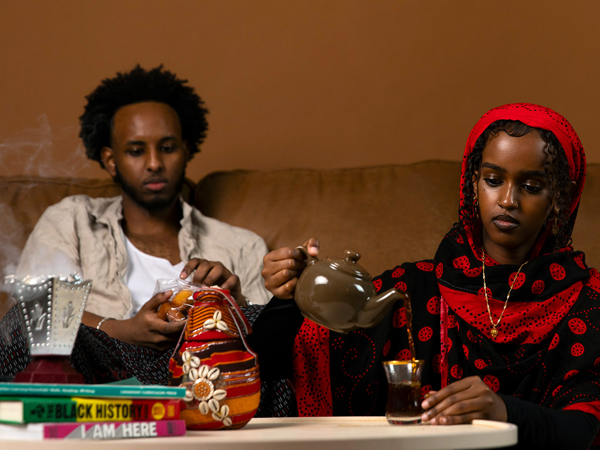 Art photography of a female pouring tea dressed in cultural garments and a male eating