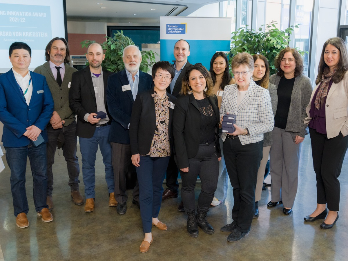 Faculty and staff pose for a photo with their awards in hand in front of a teal banner with the Toronto Metropolitan University banner