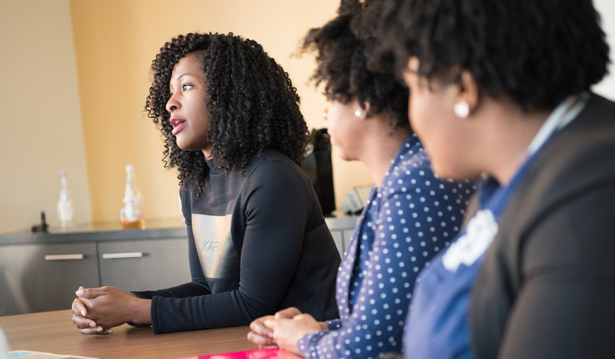 Three Black women talk around a meeting room table.