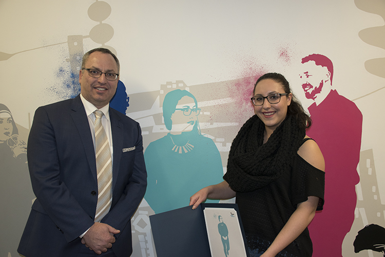 A woman with the Dean standing in front of a colourful mural of students