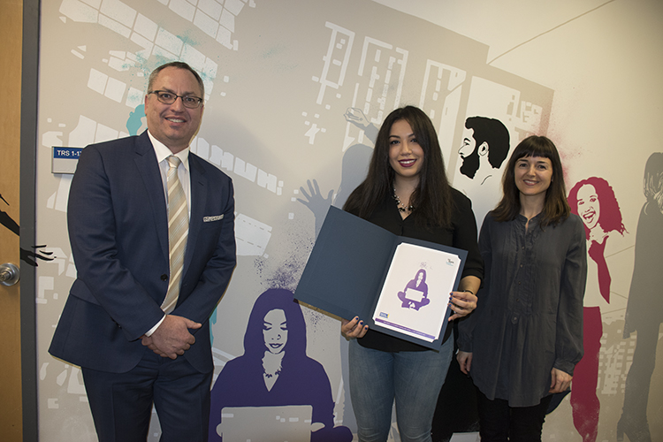 Dean Steve Murphy posing with a young woman holding a certificate in front of a colourful mural