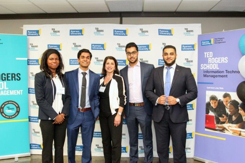 Five female and male students pose in front of a TRSM media wall at a ryerson event