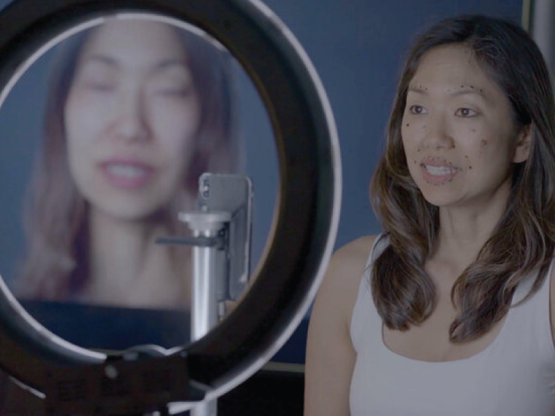 Filmmaker Ann Shin sits in front of a propped cell phone capturing her facial expressions