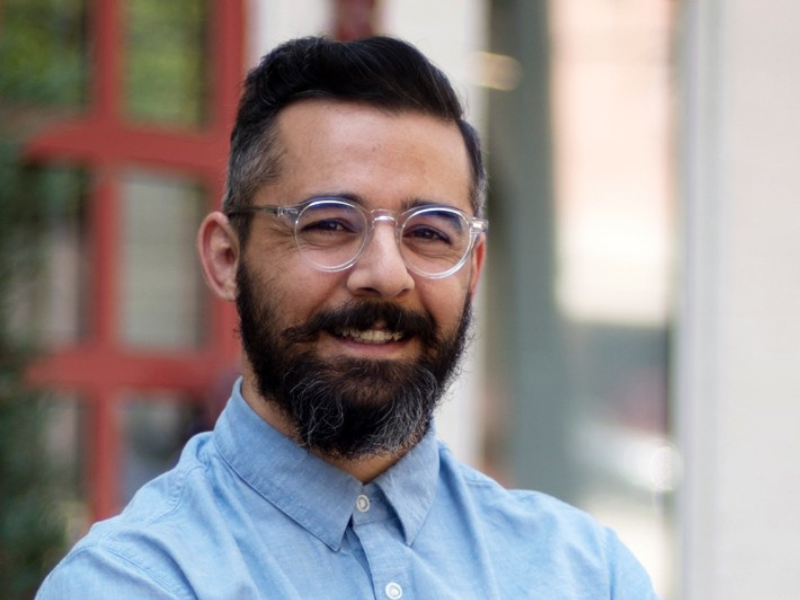 Dr. David Colangelo, wearing clear glasses and blue button-up shirt, looks directly at camera