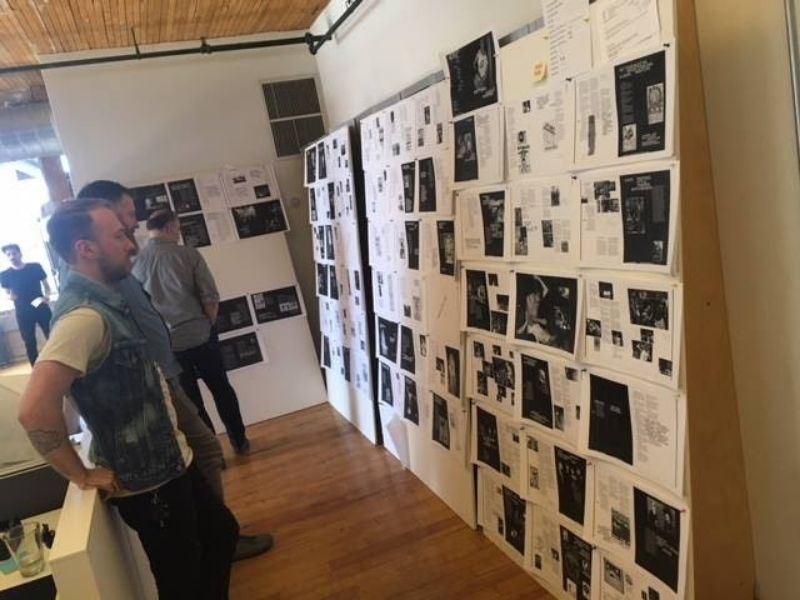 Three people standing and staring at a wall of black and white cut out pages