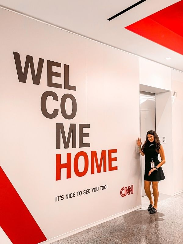 Young woman in a black dress leans against a wall with the words 'Welcome Home'