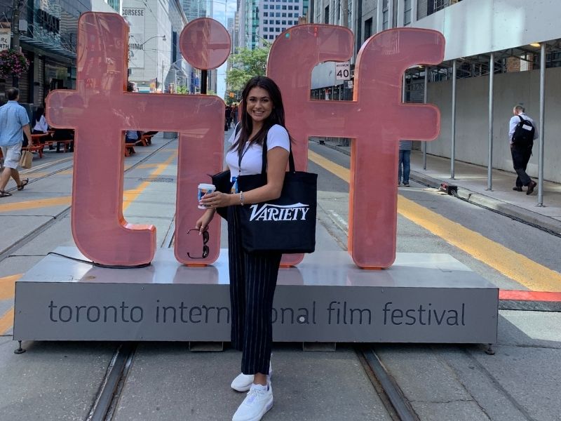 Young woman stands in front of large TIFF sign on street