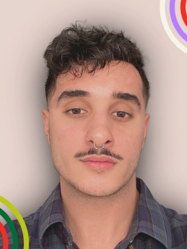 Headshot of a young man with dark short hair , slight moustache and silver nose ring