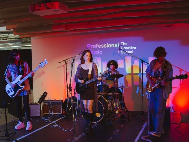 A crowd of people look toward a band performing on a brightly lit stage.