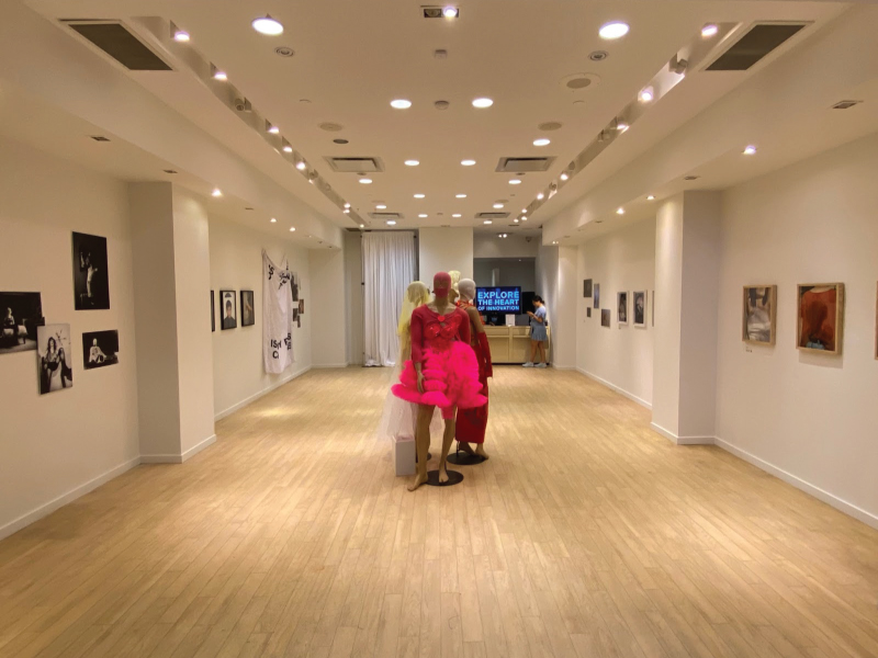 Image of the exhibition, A Measure of Being, with fashion on mannequins in the centre of the room alongside a variety of photographs, video and mixed media