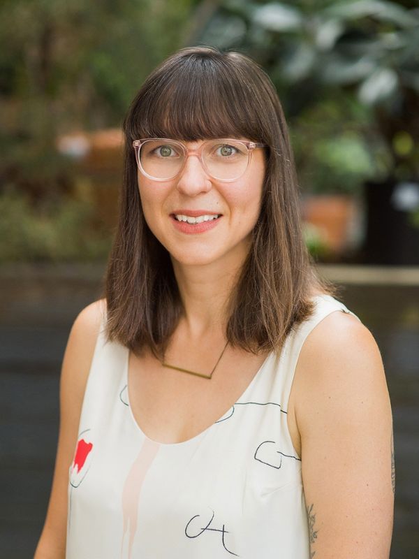 A woman with brown hair wearing glasses smiling.