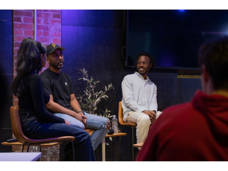 Three people sitting down in a darkly lit room caught in the middle of a lively conversation.