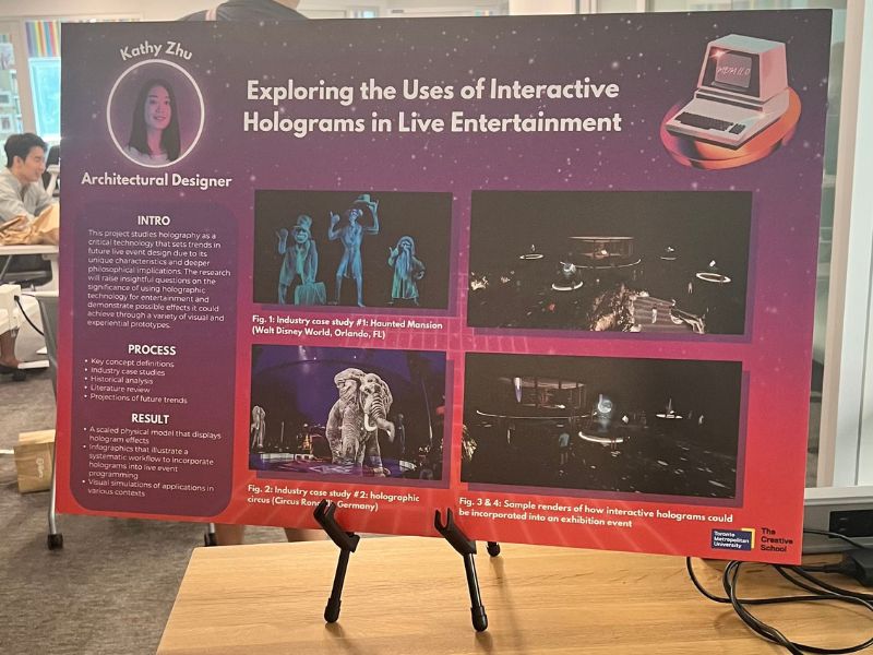 A display sign with information about holograms in live entertainment stands on a table with a woman standing enthusiastically beside it