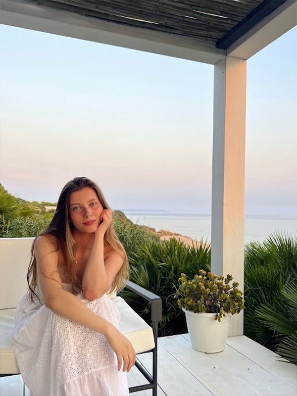 A woman wearing a dress sitting down on a bench overlooking a scenic ocean view