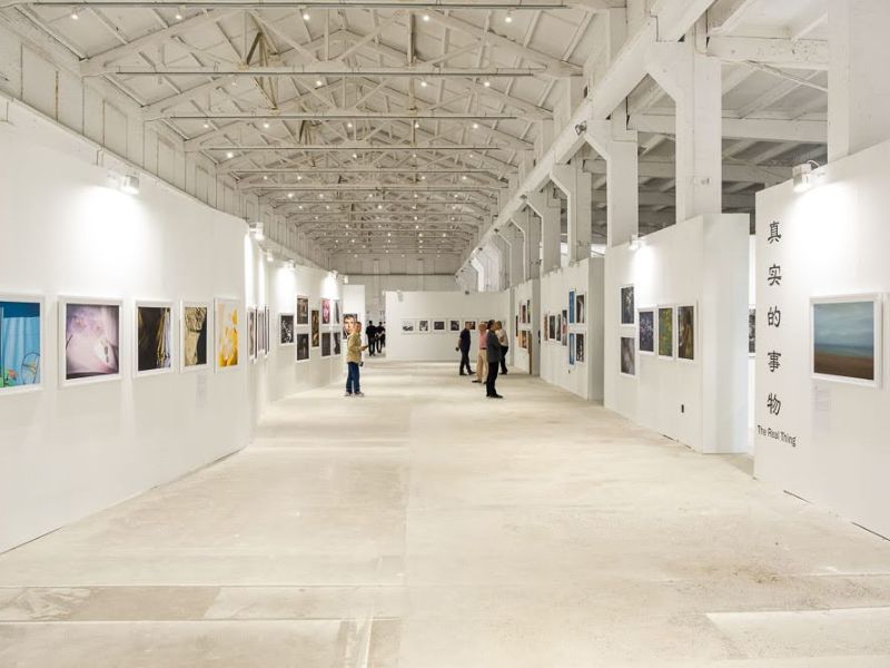 A brightly lit studio space featuring photographs hung on the walls and tourists examining the work.