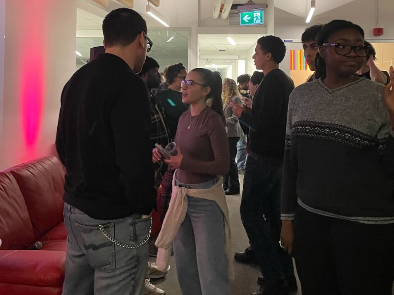 Students and panellists stand around around the room talking to one another.