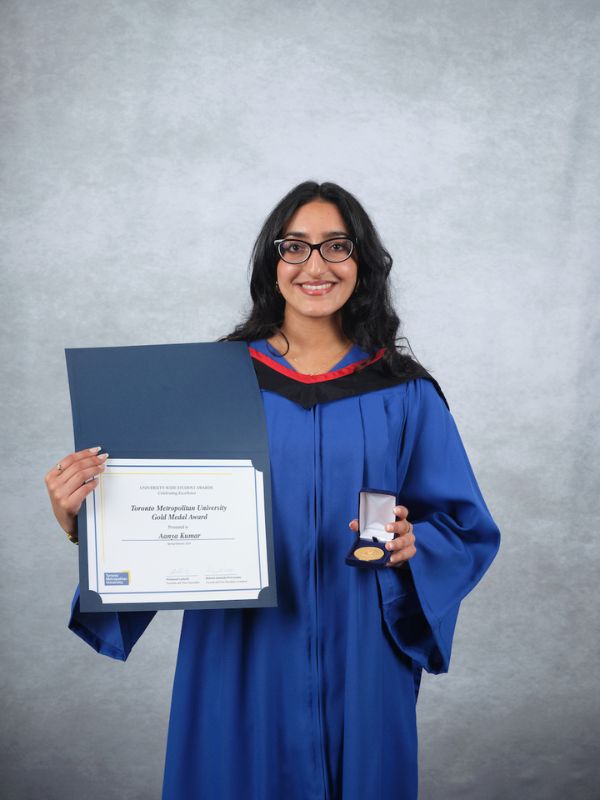 Woman wearing glasses and graduation gown holding a certificate and gold medal