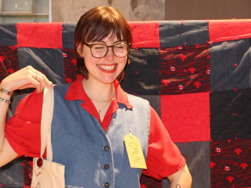 A guest models their custom tote bag in front of a backdrop made of upcycled denim and red fabric squares