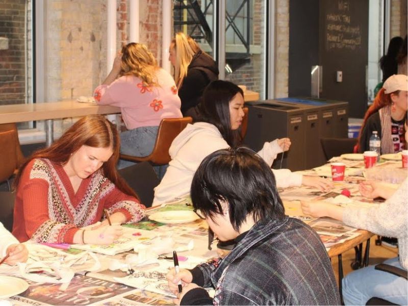 Guests sit at a table to decorate their own tote bags using markers, ribbons, and buttons