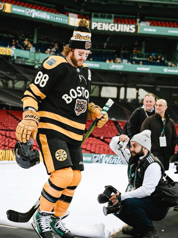 A man kneels down to take a picture of a hockey player skating off the ice. Two men are smiling in the background looking off screen