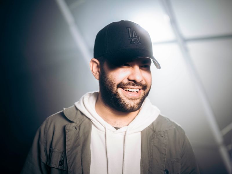 A man wearing a black hat with the words LA written on it. A light is shining from behind the subject, casting a shadow across part of the mans face