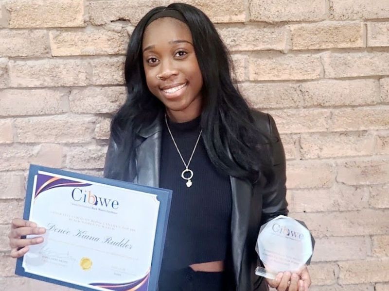 Denee Rudder standing in front of a brick wall holding a CIBWE certificate and award