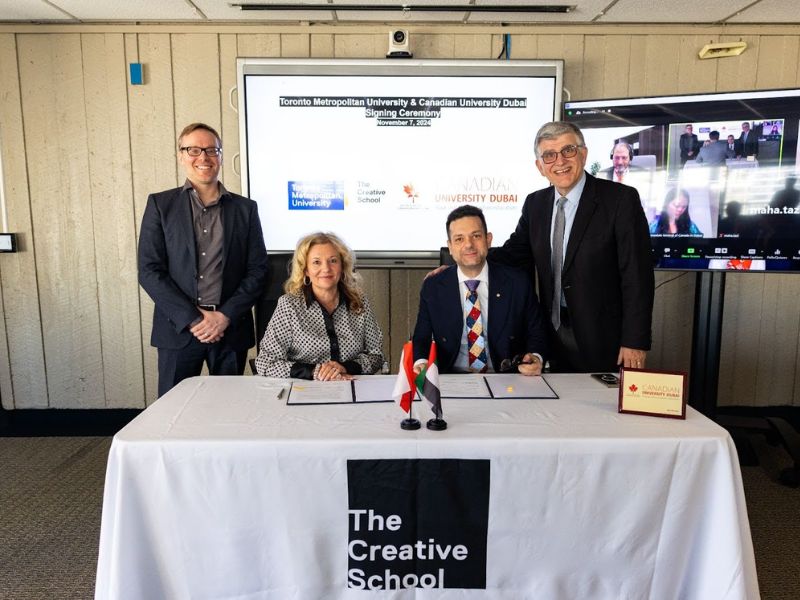 Four people pose together at a signing ceremony between Toronto Metropolitan University and Canadian University of Dubai. Two of the individuals are seated at a table with documents in front of them, and behind them two other individuals stand smiling. 