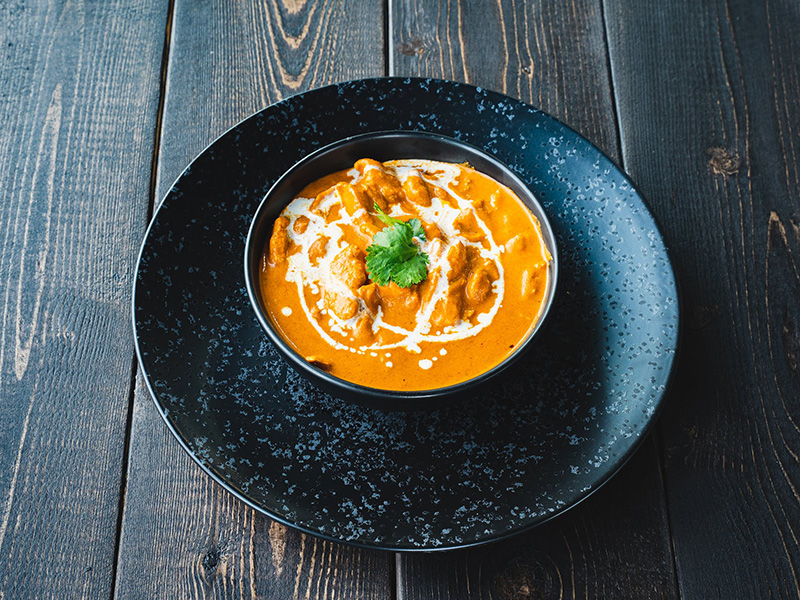 TMU Eats catering menu butter chicken in a black stoneware bowl on top of a matching plate.