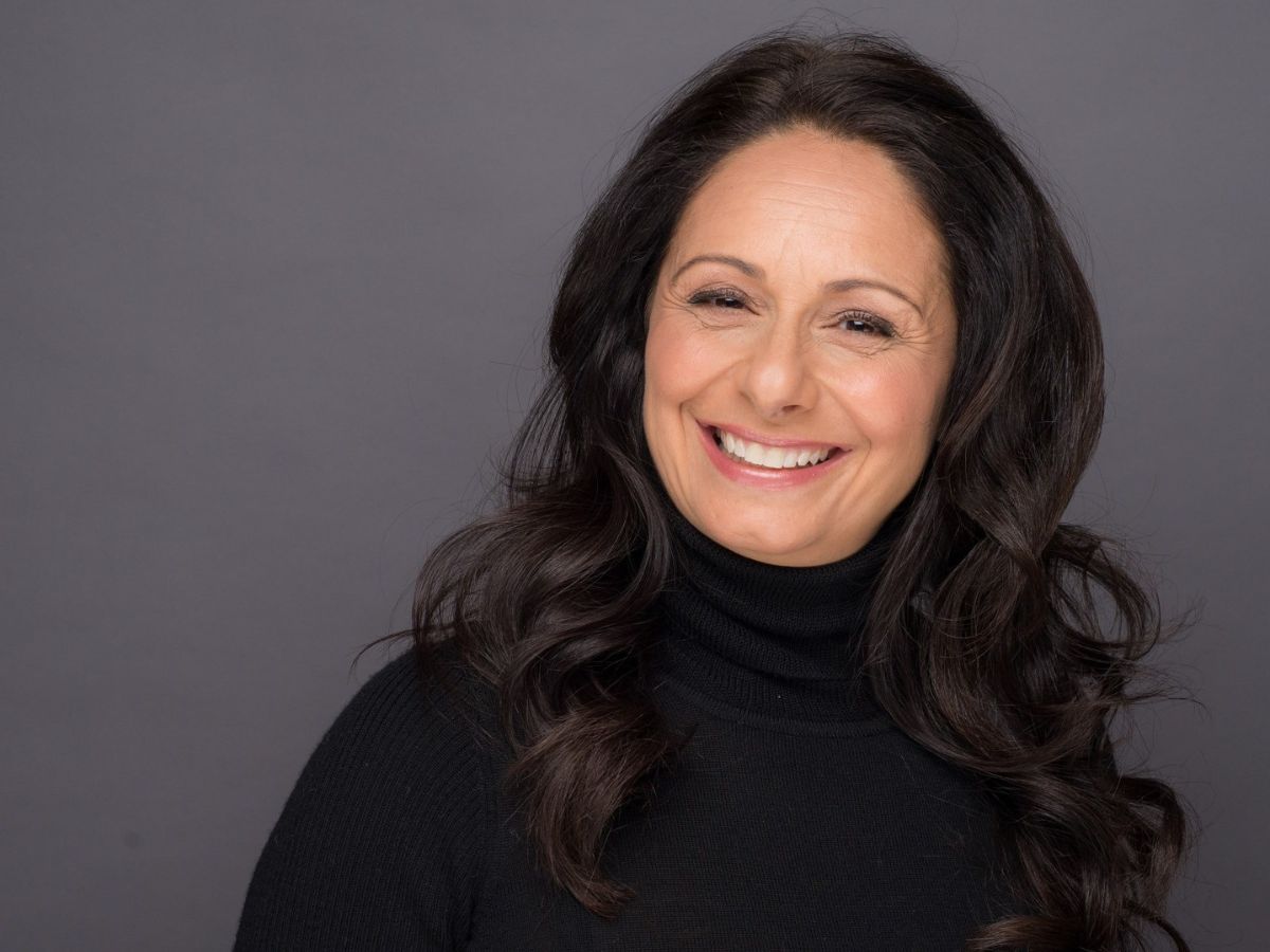 Headshot of woman with dark hair smiling with grey backdrop