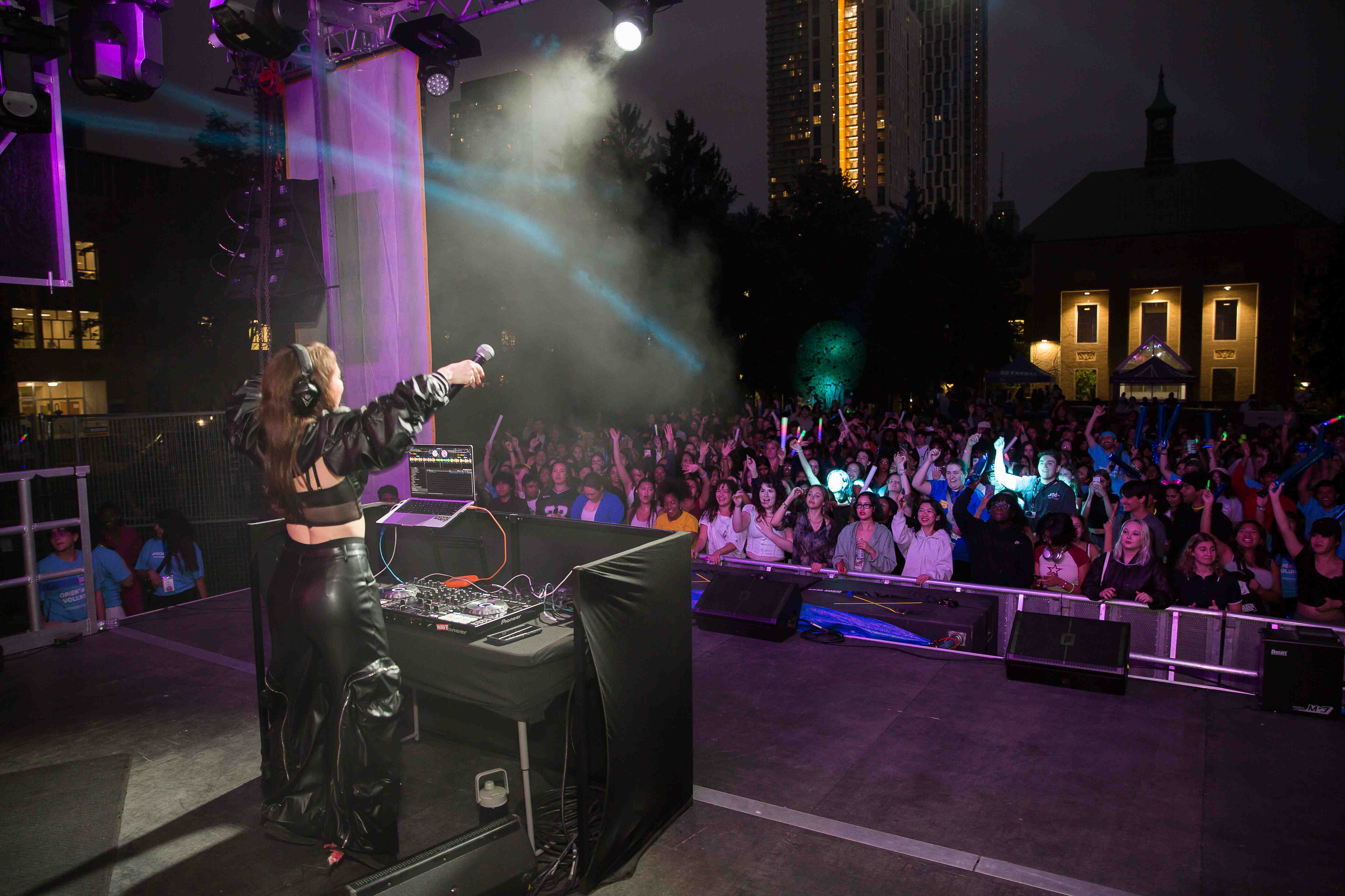 Stage view of DJ on a stage in front of a crowd of students at Kerr Hall Quad, Orientation Week.