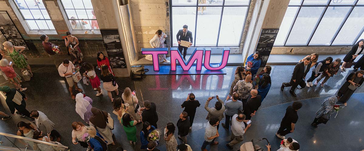 Graduates and guests walk in the concourse of the Mattamy Athletic Centre, in front of "TMU" illuminated letters.